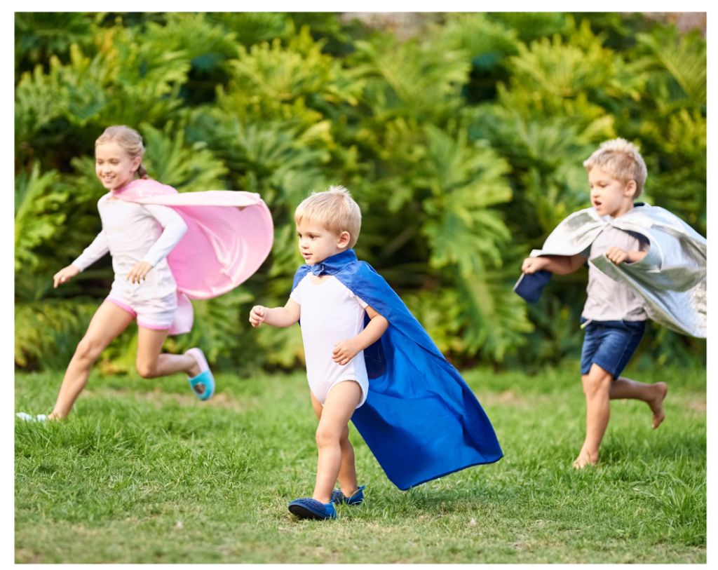 Three children with capes, running across a green field